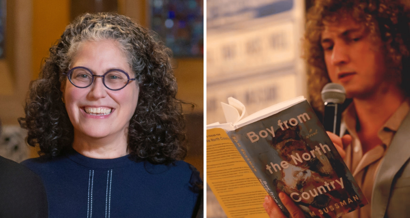 A smiling woman stands beside a man reading aloud from the book Boy from the North Country by Sam Sussman at Temple Emanu-El.