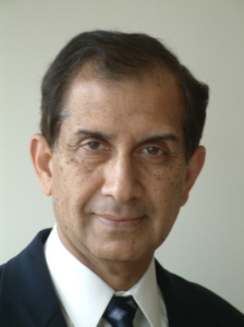 A well-groomed man in a suit and tie with short dark hair, looking at the camera against a simple background, dressed formally in a manner suitable for synagogue events at Temple Emanu-El.