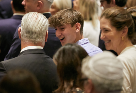 A group of congregants dressed formally, smiling and conversing together at an indoor event at Temple Emanu-El.