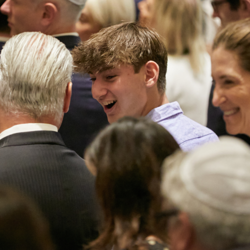 A group of congregants dressed formally, smiling and conversing together at an indoor event at Temple Emanu-El.