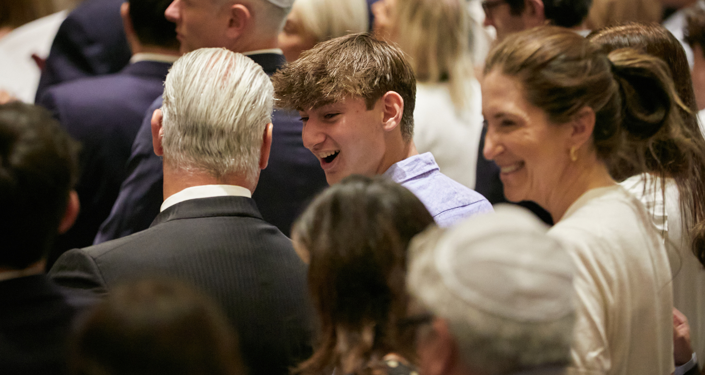 A group of congregants dressed formally, smiling and conversing together at an indoor event at Temple Emanu-El.