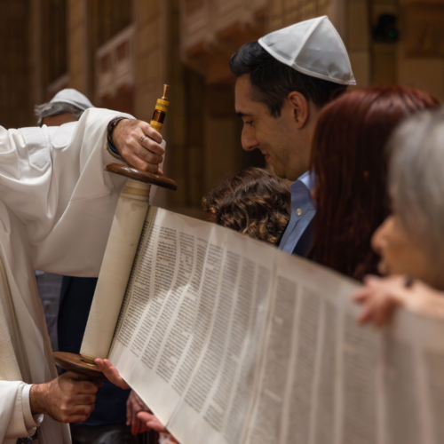 A rabbi at Temple Emanu-El unrolls a Torah scroll with congregants during a Reform Jewish service inside the synagogue’s sanctuary.