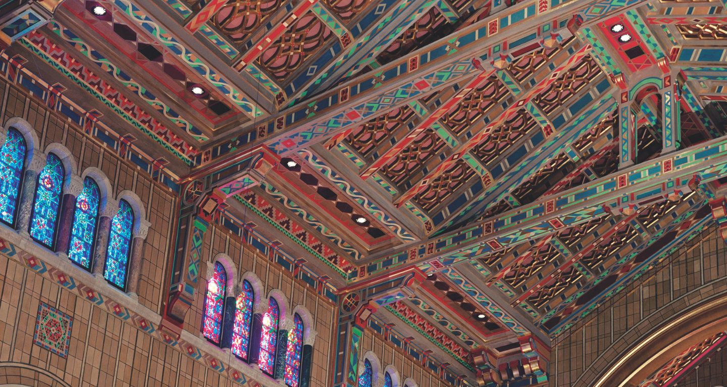 Colorful, intricately patterned ceiling and stained glass windows inside the historic sanctuary of Temple Emanu-El in New York City.
