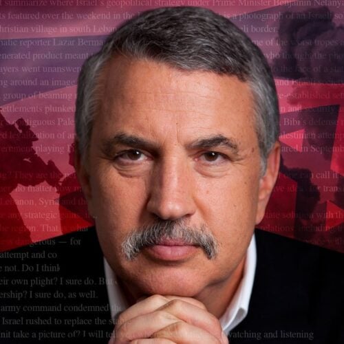 A distinguished man with gray hair and a mustache looks ahead thoughtfully, resting his hands under his chin, with a red background behind him.