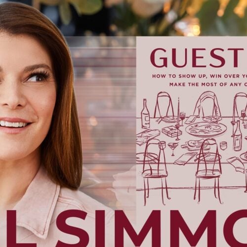 Smiling woman standing next to a book titled “Guesting,” featuring a cover illustration of a dinner table and chairs, photographed at Temple Emanu-El in New York City.