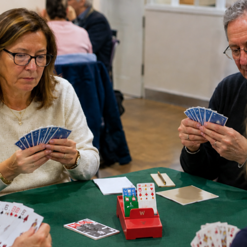 Four adults sit around a green table playing cards together in a bright, welcoming room at Temple Emanu-El.