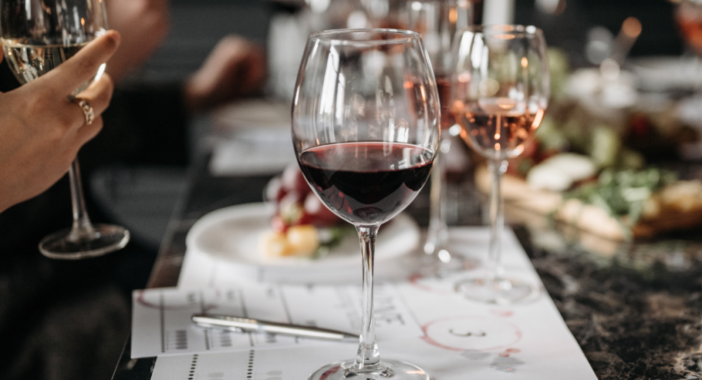 A close-up of glasses and dishes on a table set for a communal meal, with people enjoying conversation and food in the background.