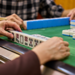 Two people playing mahjong at a green felt table, a popular social activity within the community at Temple Emanu-El.