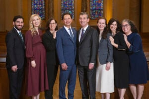 A group of eight people posing for a formal portrait inside Temple Emanu-El.