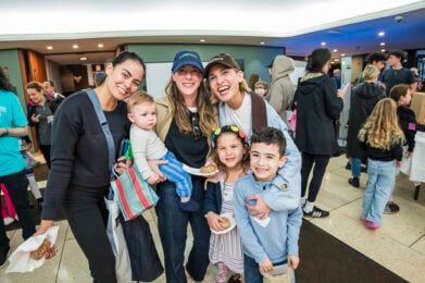 A group of parents and children smiling together at a Temple Emanu-El community event.