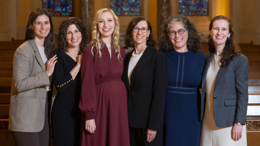 Six women in a women’s Jewish study group stand together smiling in the sanctuary of Temple Emanu-El.