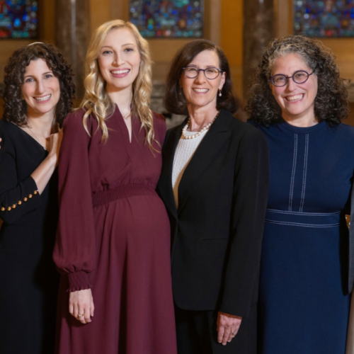 Six women in a women’s Jewish study group stand together smiling in the sanctuary of Temple Emanu-El.