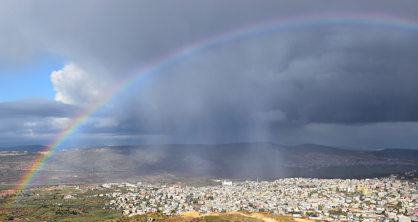 A rainbow arching over a town nestled below dark, stormy hills, symbolizing a divine covenant.