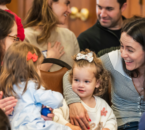 Adults and young children gather with smiles and conversation in a welcoming space at Temple Emanu-El.