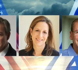 Three people stand together before a backdrop combining American and Israeli flags beneath a cloudy sky at Temple Emanu-El.