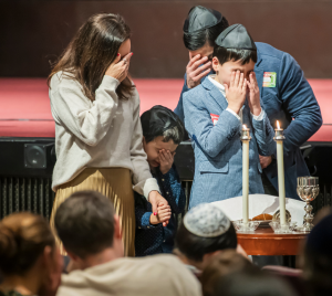 A family covers their eyes in prayer while lighting Shabbat candles at Temple Emanu-El in New York City.