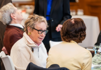 Elderly women engaged in conversation at a table during a formal gathering at Temple Emanu-El, with refreshments and attendees nearby.