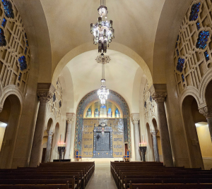 Grand Temple Emanu-El sanctuary with soaring arched ceilings, elegant stained glass, graceful chandeliers, and wooden pews.