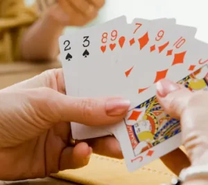 A person participates in a friendly card game at a table with others, holding a fan of playing cards.
