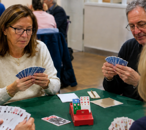 Four adults sit around a green table playing cards together in a bright, welcoming room at Temple Emanu-El.