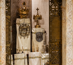 Torah scrolls adorned with elegant covers and decorative crowns displayed in a beautifully designed ark featuring detailed floral motifs at Temple Emanu-El.
