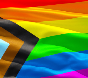 Progress Pride flag featuring rainbow stripes and chevron design on wavy fabric.