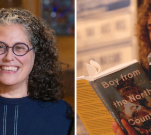 A smiling woman stands beside a man reading aloud from the book Boy from the North Country by Sam Sussman at Temple Emanu-El.
