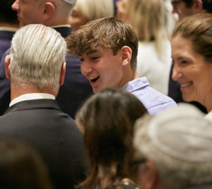 A group of congregants dressed formally, smiling and conversing together at an indoor event at Temple Emanu-El.