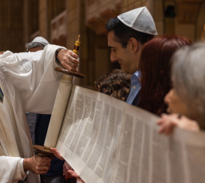 A rabbi at Temple Emanu-El unrolls a Torah scroll with congregants during a Reform Jewish service inside the synagogue’s sanctuary.