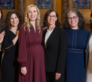 Six women in a women’s Jewish study group stand together smiling in the sanctuary of Temple Emanu-El.