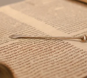 A silver yad pointer rests atop an open Torah scroll displaying handwritten Hebrew text at Temple Emanu-El in New York City.