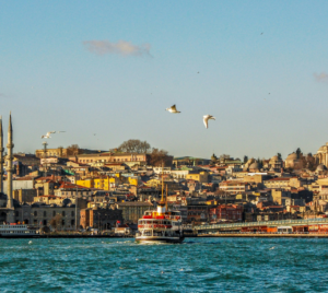 Ferries sailing on blue water with the New York City skyline in the background, including recognizable city buildings and a clear, bright sky above.
