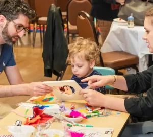 A family sits at a table in the temple, creating colorful arts and crafts together during a community event.